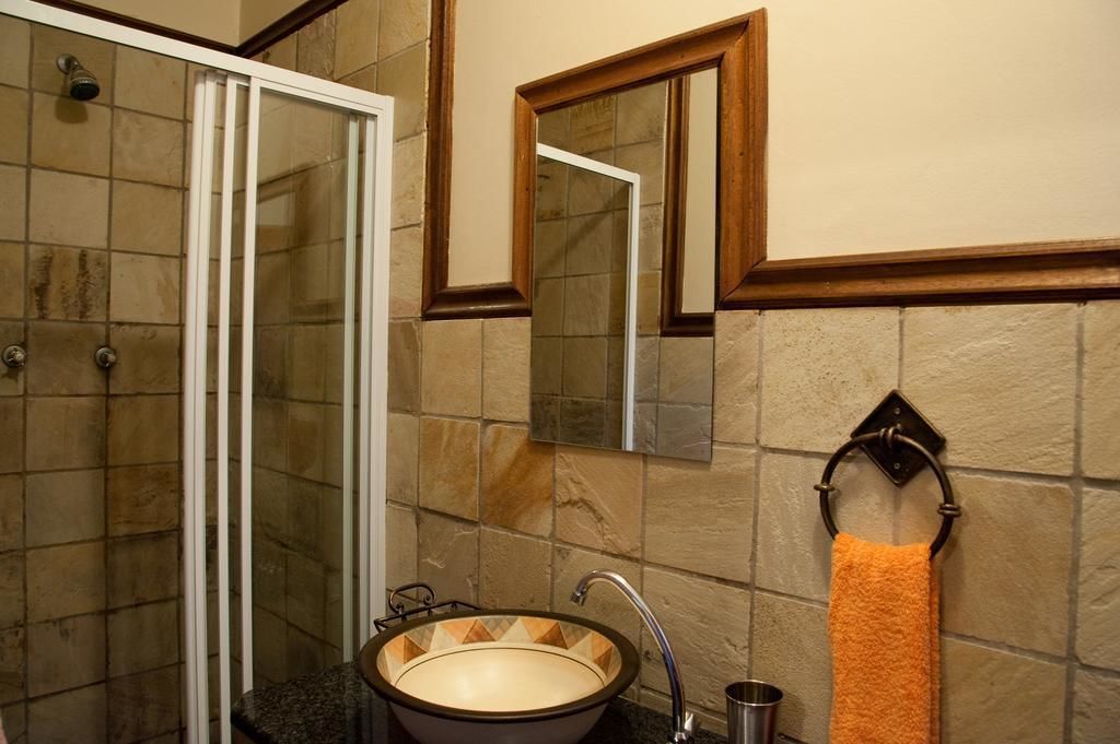 A bathroom with a glass shower enclosure, a sink with a decorative basin, a mirror, and a towel rack with an orange towel.