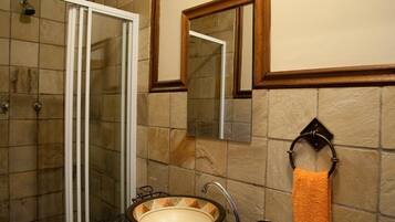 A bathroom with a glass shower enclosure, a sink with a decorative basin, a mirror, and a towel rack with an orange towel.