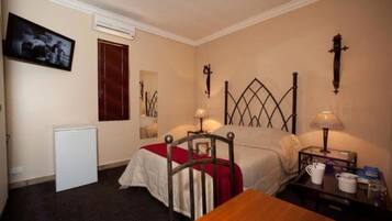 Une chambre d’hôtel avec un lit simple, des tables de chevet avec des lampes, une petite table avec une tasse et un livre, un téléviseur fixé au mur et un radiateur.