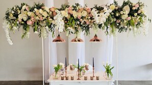 Una mesa blanca adornada con un arreglo floral, candelabros y pequeñas macetas.