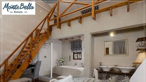 Un dormitorio con escalera de madera, un baño con un espejo grande y una cama con toallas enrolladas.