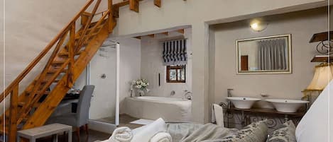 Un dormitorio con escalera de madera, un baño con un espejo grande y una cama con toallas enrolladas.
