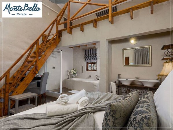 Une chambre avec un escalier en bois, une salle de bain avec un grand miroir et un lit avec des serviettes enroulées.