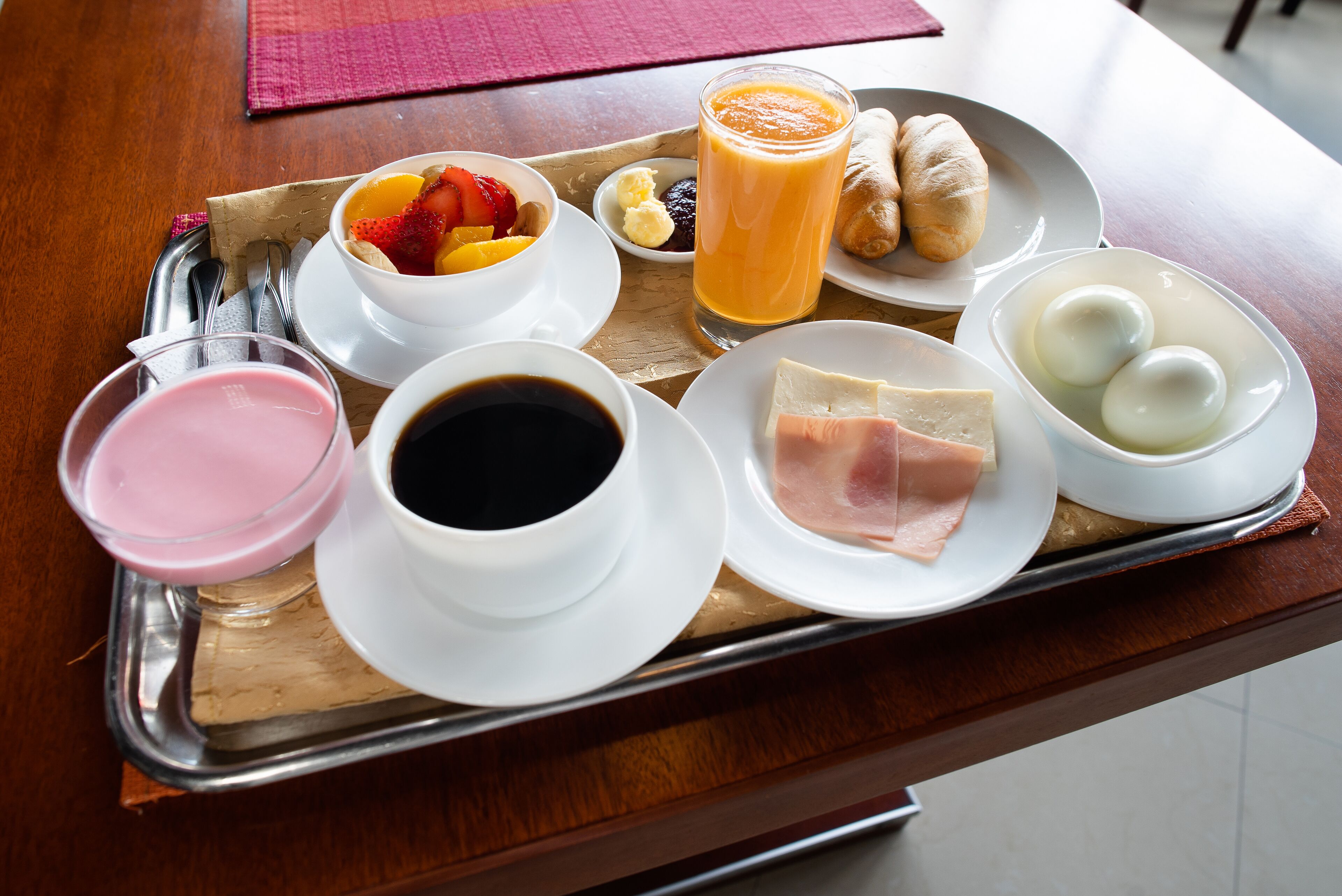 A tray with breakfast items including eggs, ham, juice, and pastries.