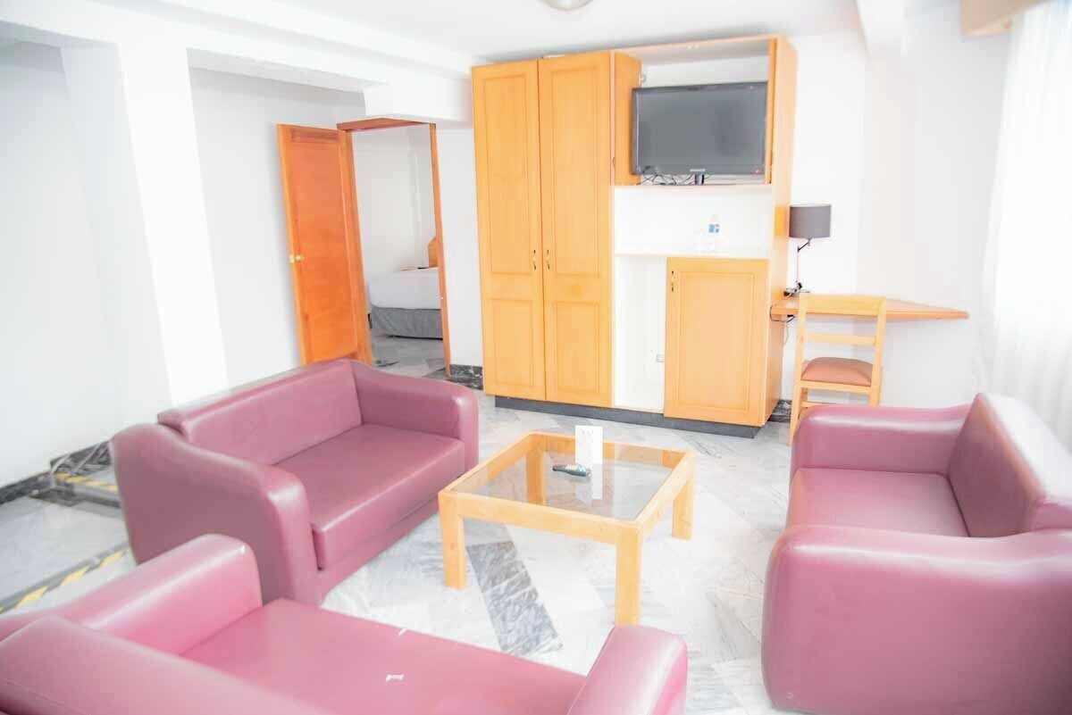 Una sala de estar con dos sofás rosa, una mesa de centro de vidrio y armarios de madera.