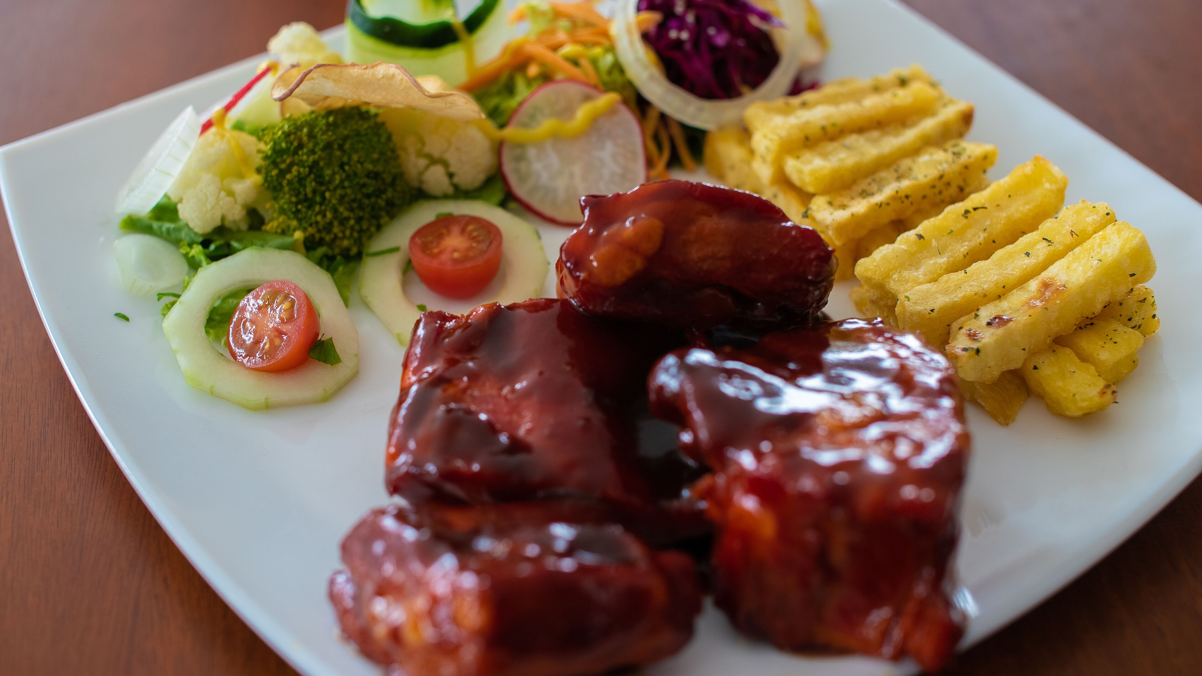 A plate of food with ribs, fries, and a salad.
