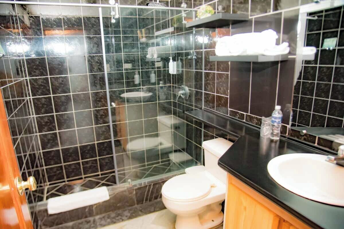 A modern bathroom with a glass-enclosed shower, a white toilet, and a black countertop with a sink.