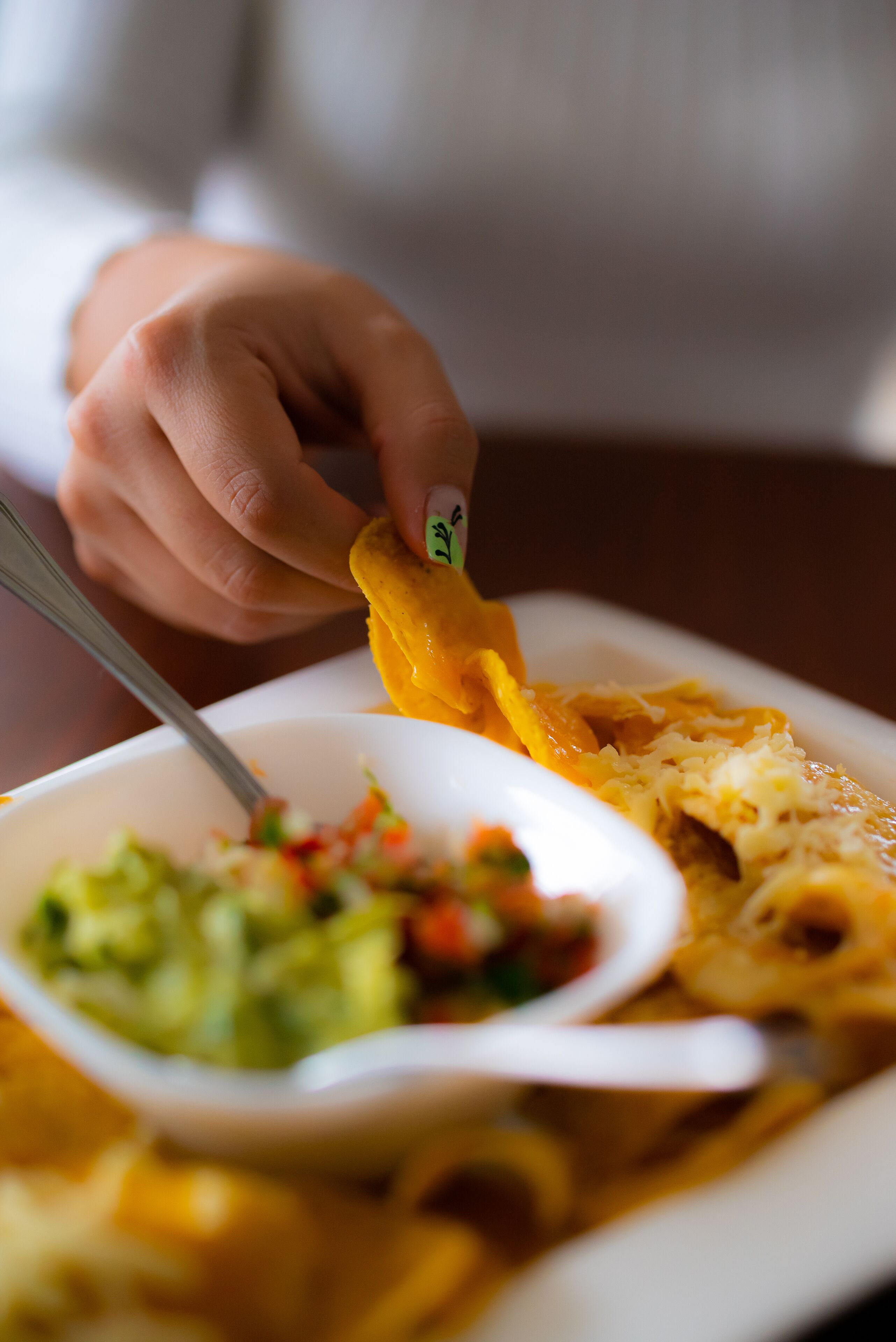 Una persona sosteniendo una tortilla sobre un plato con un tazón de guacamole y salsa.