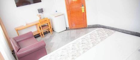 Una habitación con cama, escritorio, silla y televisión en la pared.