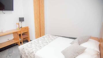 Un dormitorio con cama, escritorio, silla, televisor montado en la pared y panel de madera en la pared.