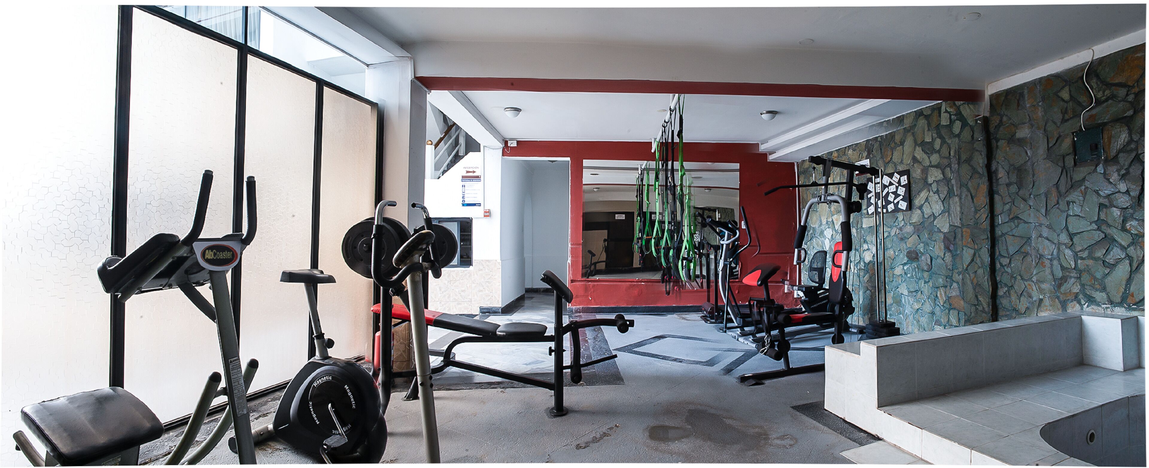Un gimnasio con equipo de ejercicio, una pared de piedra y una pared de acento roja.