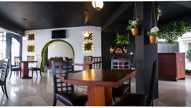 Un interior de restaurante moderno con mesas y sillas de madera, patrones decorativos en las paredes y plantas colgantes.