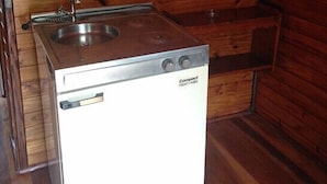 Pieni, käytännöllinen keittiö, jossa on liesi, pesuallas ja säilytystilaa, ja se sijaitsee puurakenteisessa mökissä.