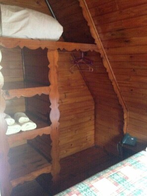 A wooden interior with a bunk bed, a small shelf with shoes, and a patterned bedspread.