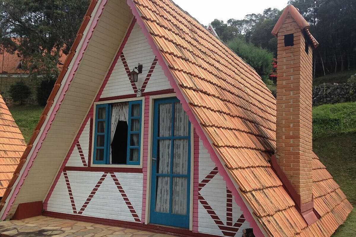 A small, triangular-shaped building with a steeply pitched roof, a chimney, and a window with blue shutters.