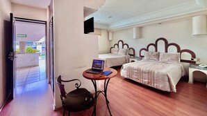 Habitación de hotel con dos camas, un escritorio con una computadora portátil, una silla y un televisor montado en la pared.