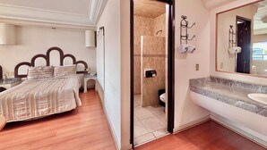 Una habitación de hotel con cama, baño con lavabo y espejo, y ducha.
