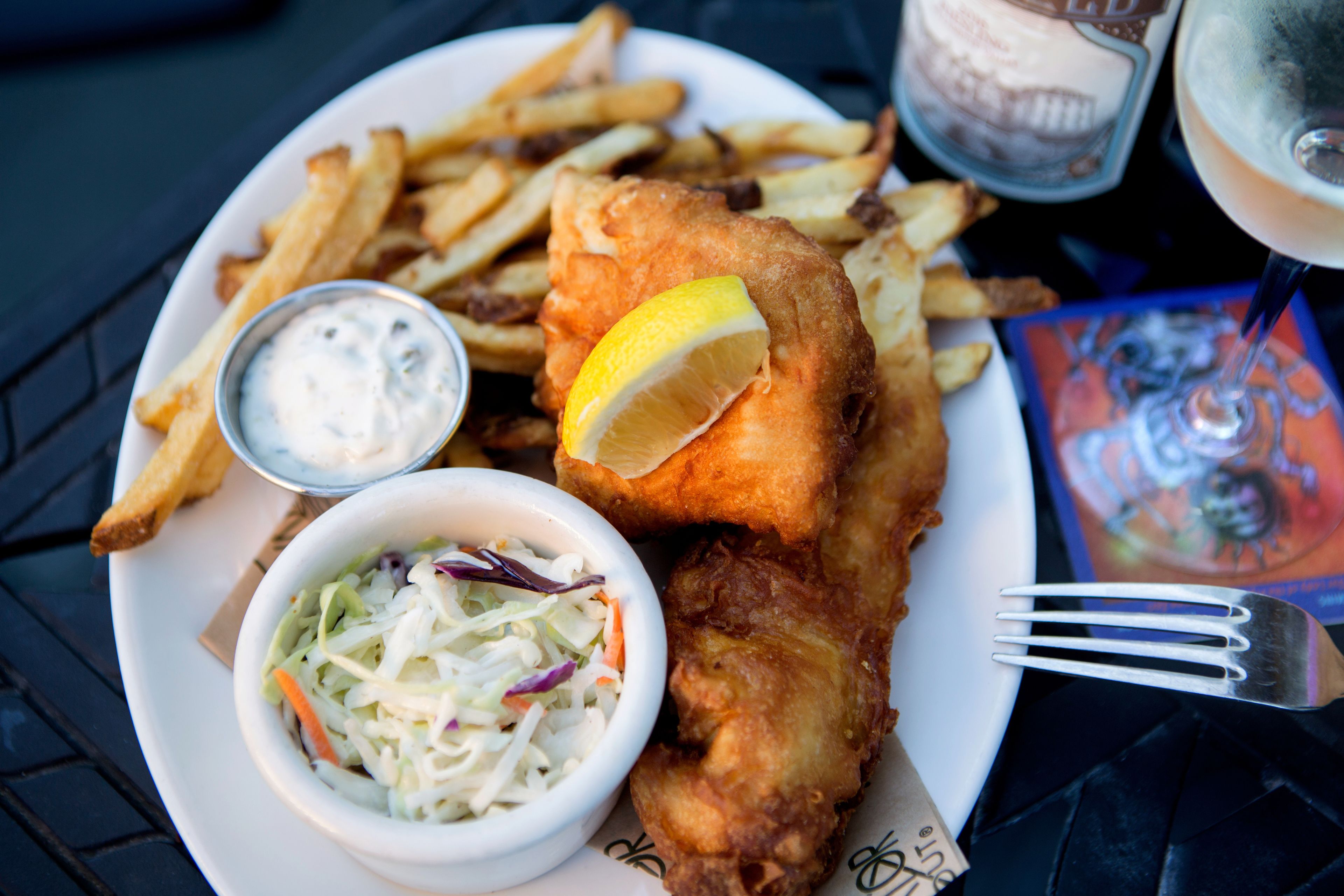 Ein Teller mit Fisch und Pommes, eine kleine Schüssel Krautsalat und ein Getränk.