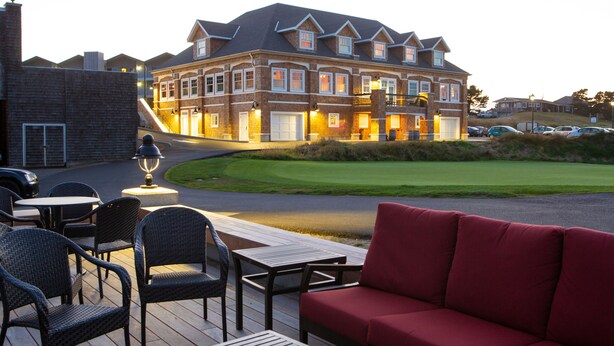 A large brick building with multiple windows and a garage, a deck with outdoor furniture, and a green lawn in the foreground. - McMenamins Gearhart Hotel (Gearhart)