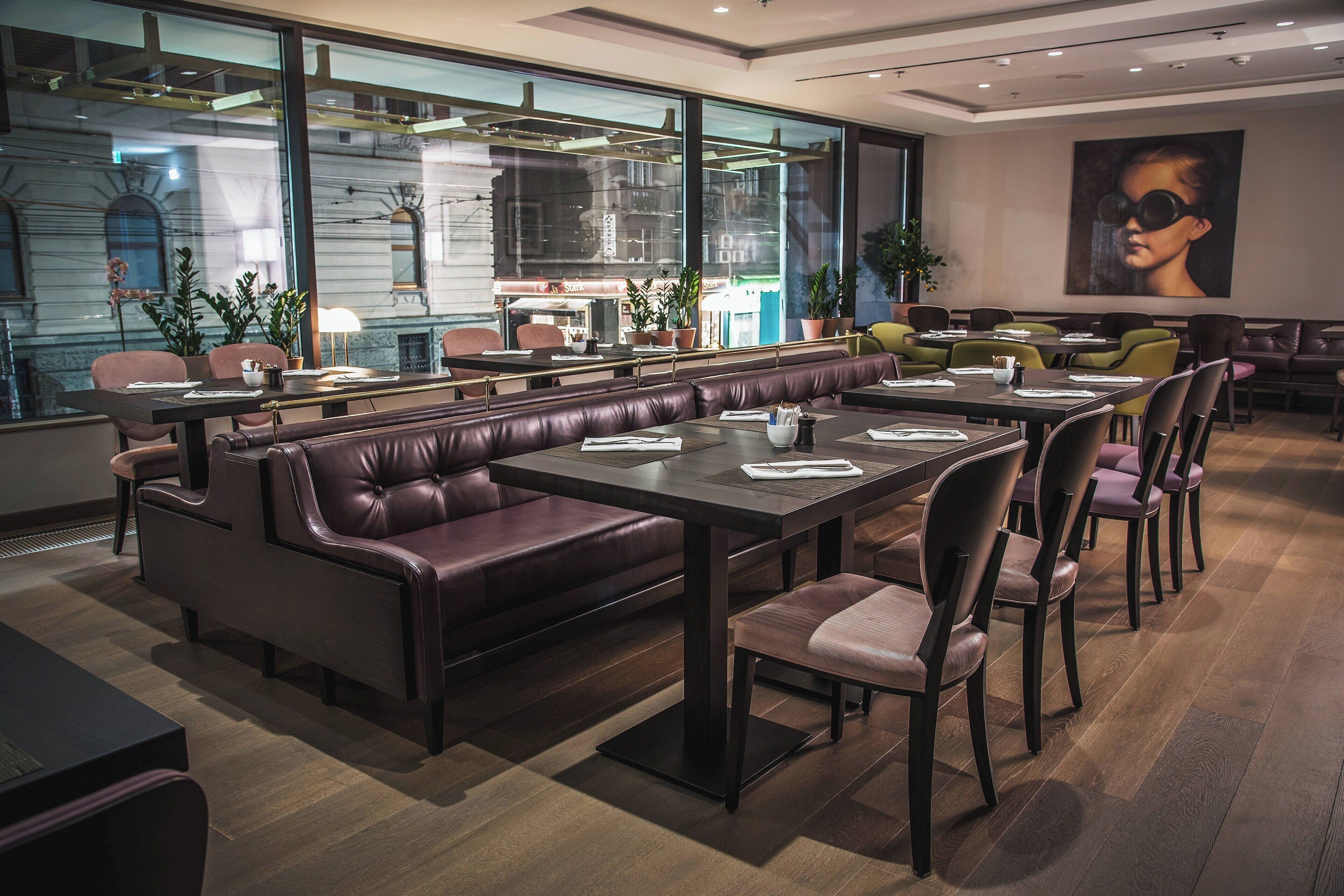 Un restaurant moderne avec des banquettes en cuir, des tables et des chaises en bois. De grandes fenêtres offrent une vue sur le paysage urbain.