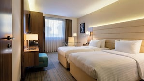 Een hotelkamer met twee bedden, een bureau met lamp, een televisie en een raam met gordijnen.