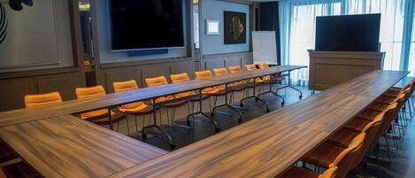 A conference room with a long wooden table, orange chairs, a large flat-screen TV, and a whiteboard.