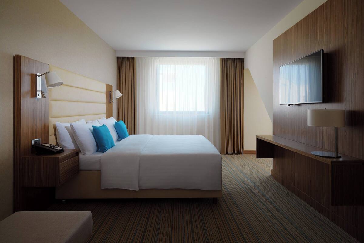 Ein Hotelzimmer mit Bett, Fernseher, Schreibtisch und einem Fenster mit Vorhängen.