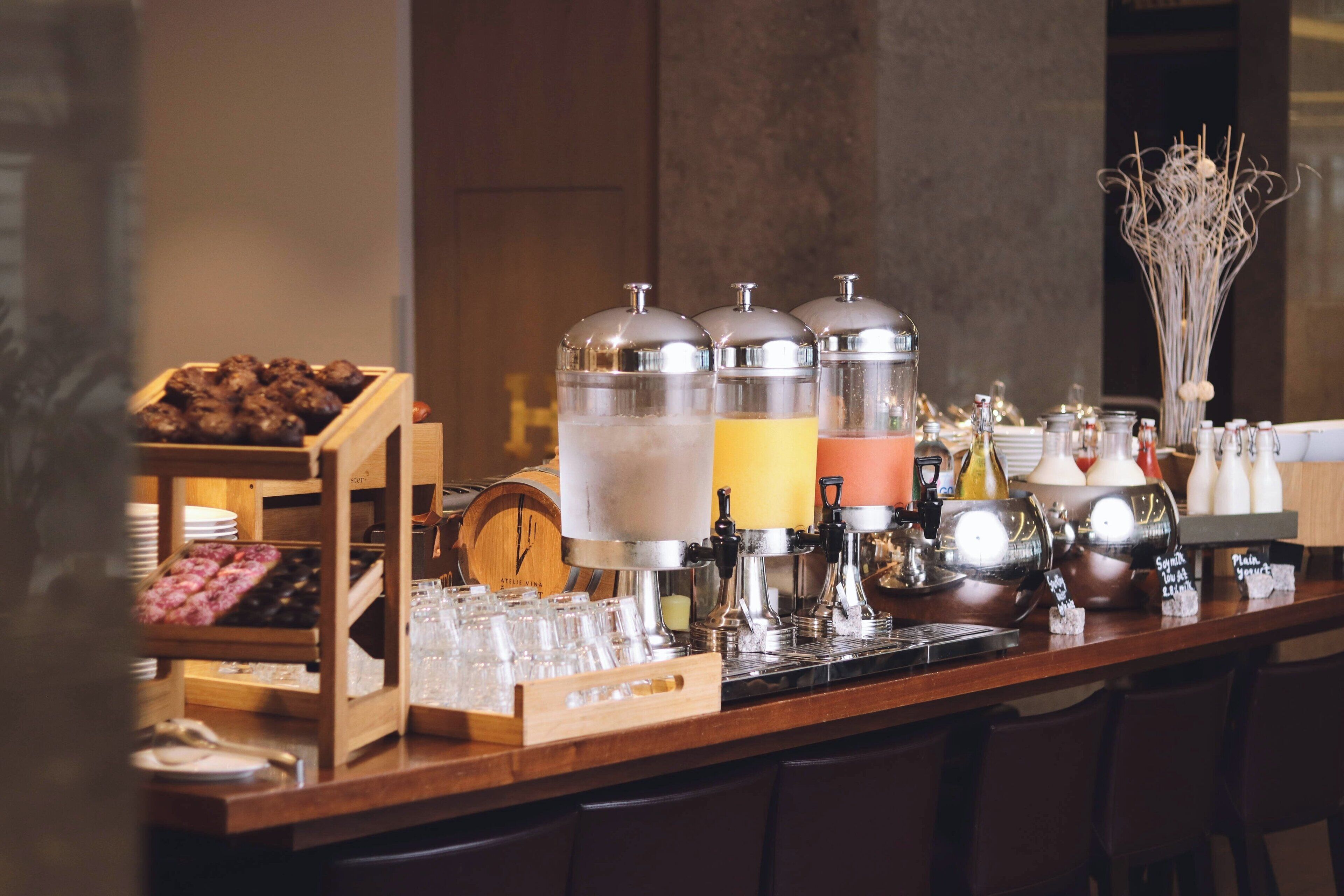 Una zona de bar con una máquina de café, una presentación de frutas y una variedad de vasos.