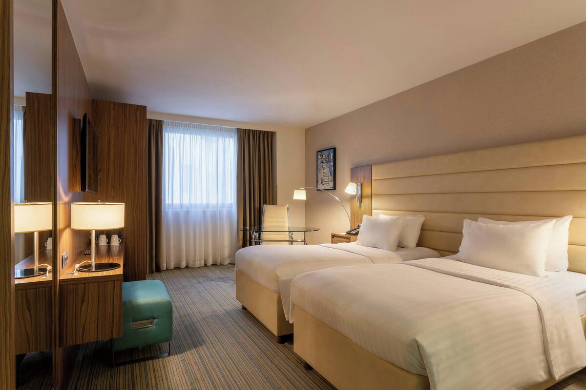 Ein Hotelzimmer mit zwei Betten, einem Schreibtisch mit Lampe, einem kleinen Tisch und einem Stuhl.