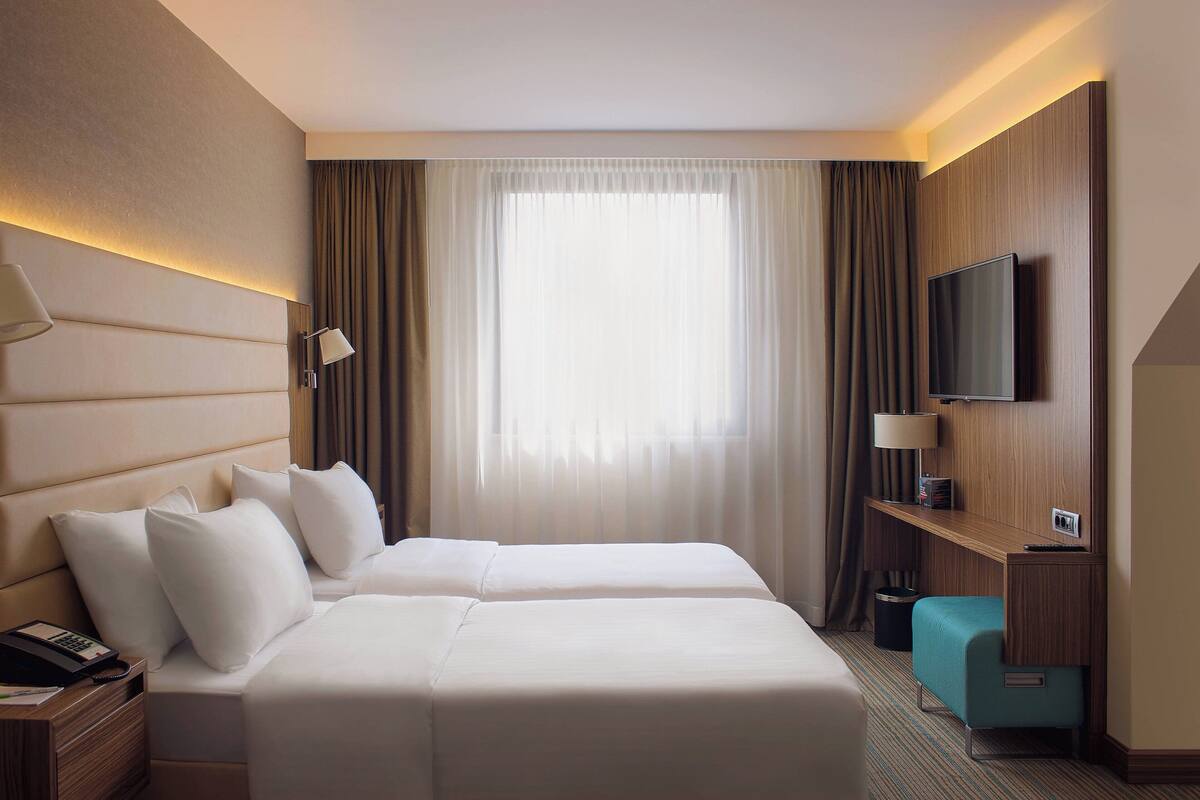 Ein Hotelzimmer mit zwei Betten, einem Fernseher, einem Schreibtisch und einem Fenster mit Vorhängen.