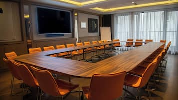 A conference room with a long wooden table, orange chairs, a large screen, and a whiteboard.