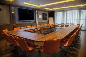 A conference room with a long wooden table, orange chairs, a large screen, and a whiteboard.