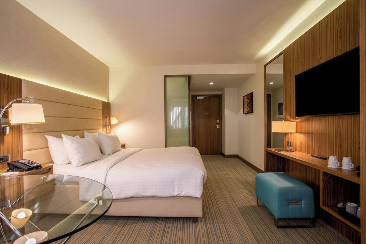 Ein Hotelzimmer mit Bett, Nachttisch, Lampe, Fernseher und einer kleinen Sitzecke.