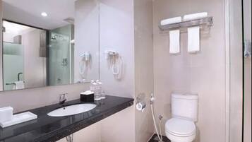 A modern bathroom with a black countertop sink, a large mirror, a toilet, and a glass-enclosed shower area.