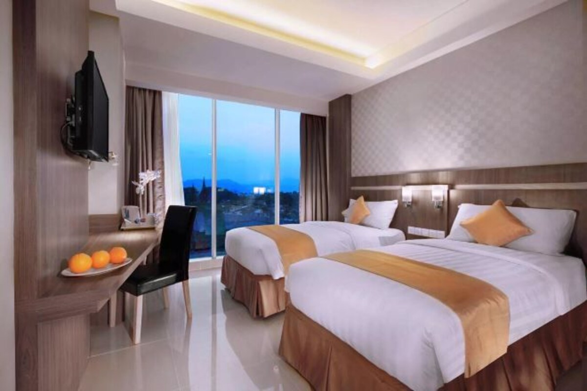 A hotel room with two beds, a desk with a chair, a TV, and a large window with a city view.