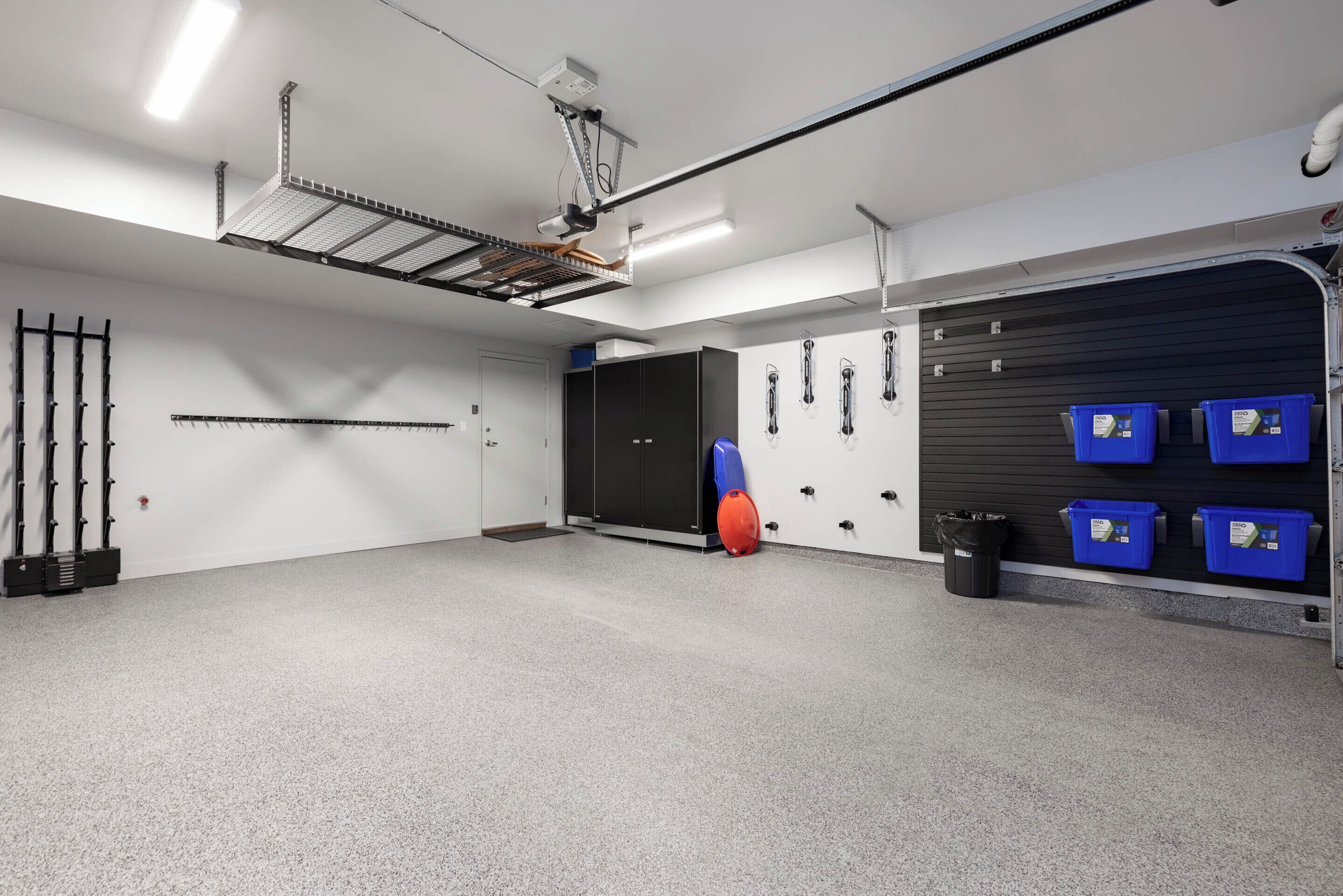 A clean, well-lit garage with a ceiling-mounted drying rack, black cabinets, and blue storage bins.