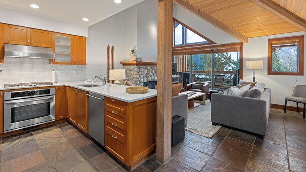 A modern kitchen with wooden cabinets, a large island, and a stone backsplash. - Montebello by Whistler Premier (Whistler)