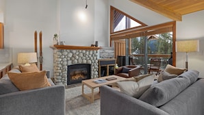 A cozy living room with a stone fireplace, comfortable seating, and large windows offering a view of the outdoors. - Montebello by Whistler Premier (Whistler)