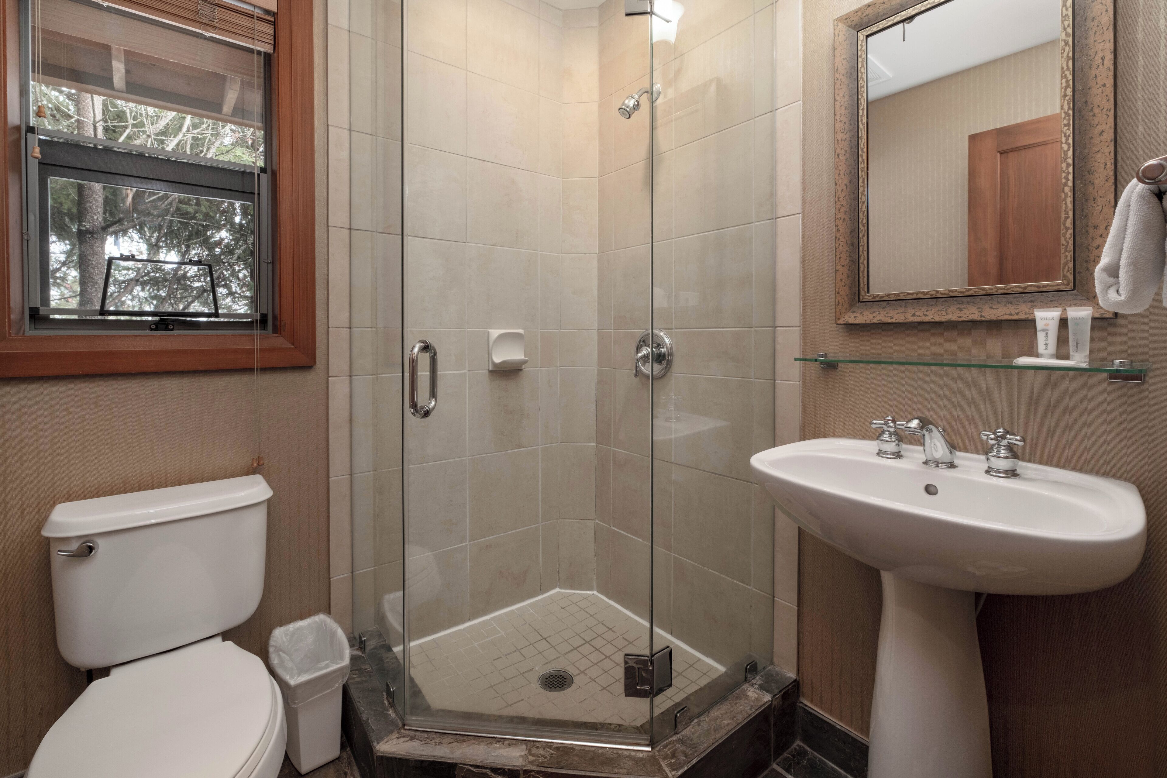 A bathroom with a glass-enclosed shower, a toilet, and a pedestal sink.