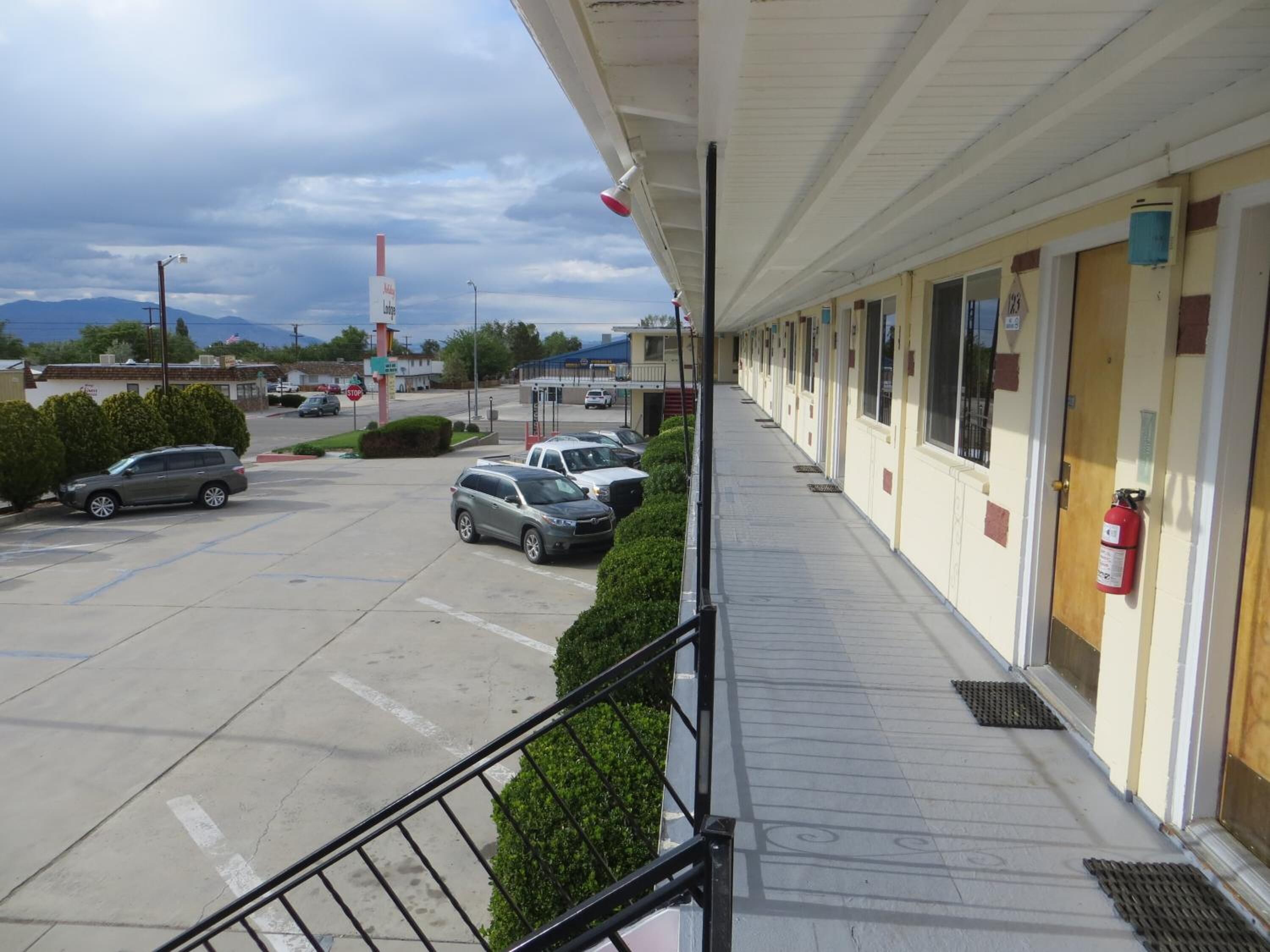 A motel with a covered parking area, a fire extinguisher mounted on the wall, and a clear view of the street and mountains in the background.