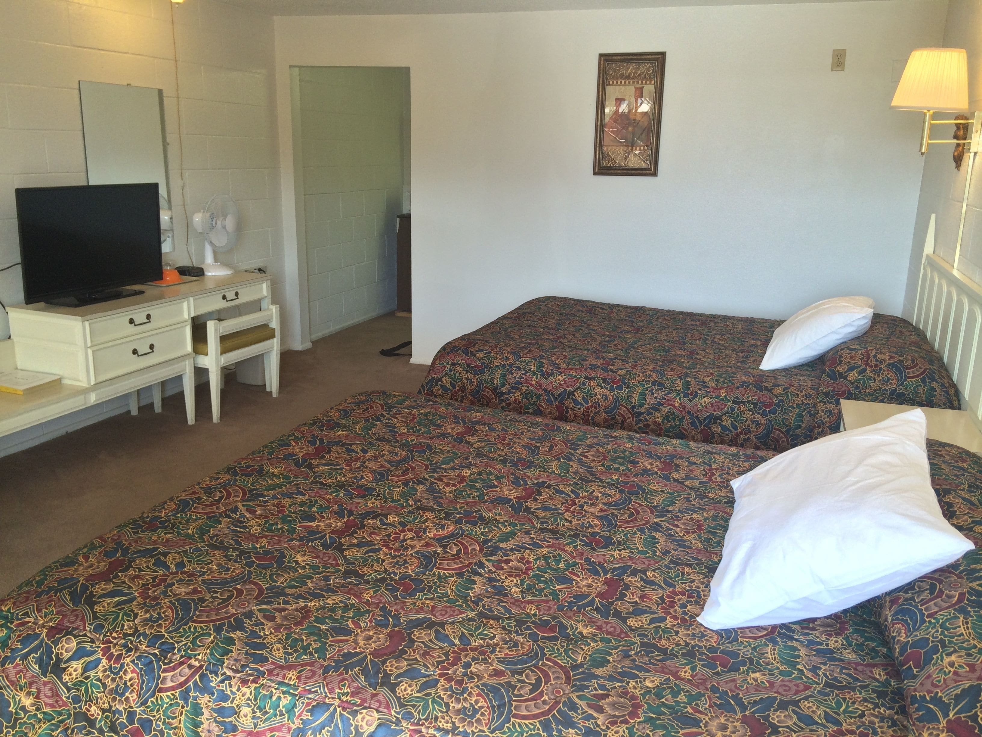 A hotel room with two beds, a desk with a television, a chair, and a lamp.
