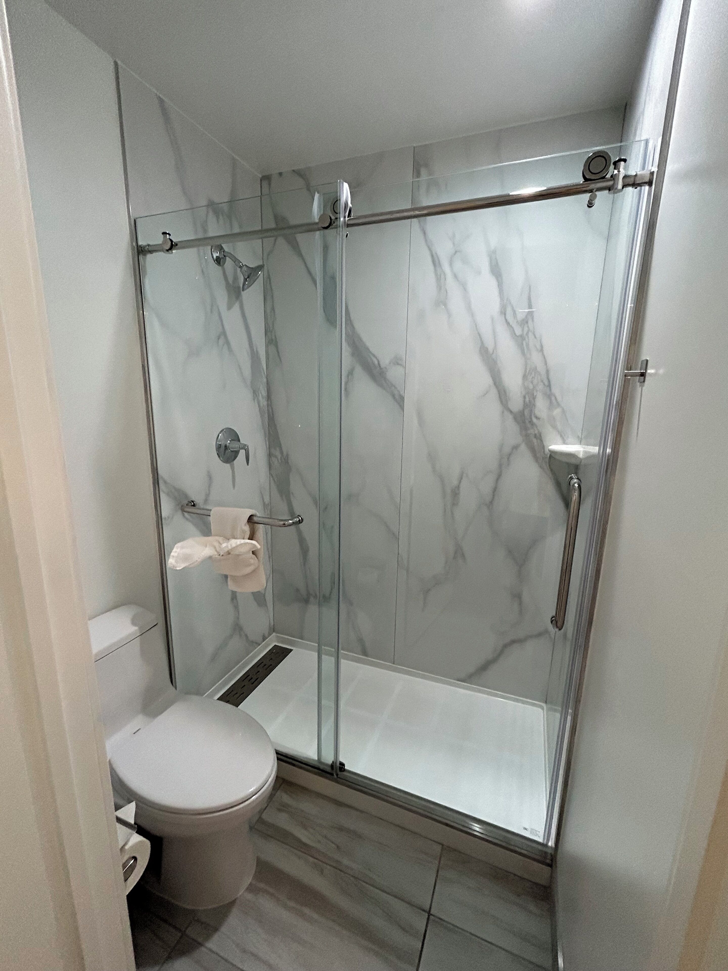 A modern bathroom with a glass-enclosed shower, a toilet, and a marble backsplash.