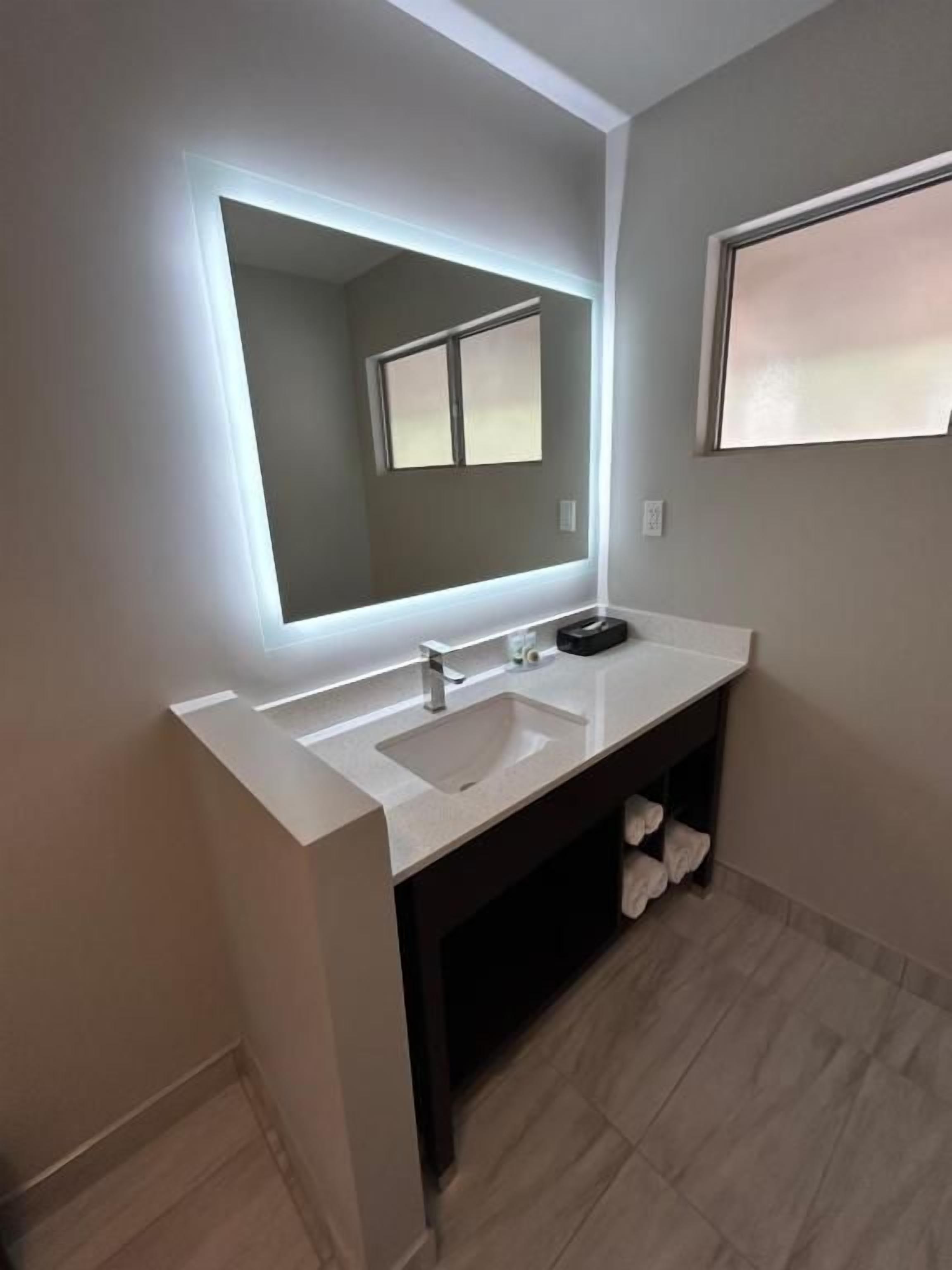 A modern bathroom with a large mirror, a white sink, and a dark cabinet.