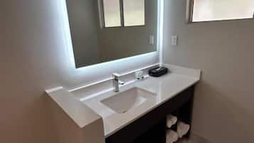 A modern bathroom with a large mirror, a white sink, and a dark cabinet.