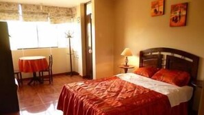 Una habitación de hotel con cama, una mesa y sillas, una lámpara y obras de arte en la pared.