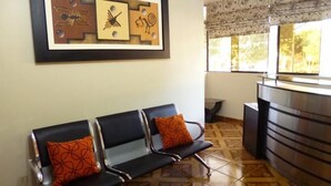 Un área de recepción con mostrador, tres sillas negras con cojines de estampado naranja y una pared con arte abstracto.