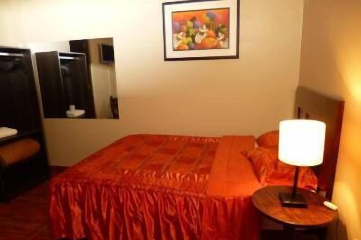 Ein Hotelzimmer mit einem großen Bett, einem Nachttisch mit Lampe, einem Spiegel und einem Bild an der Wand.