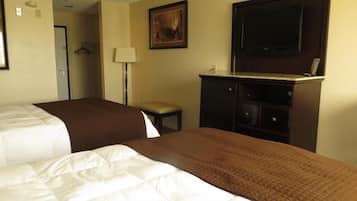 A hotel room with two beds, a desk, a chair, a lamp, and a television.