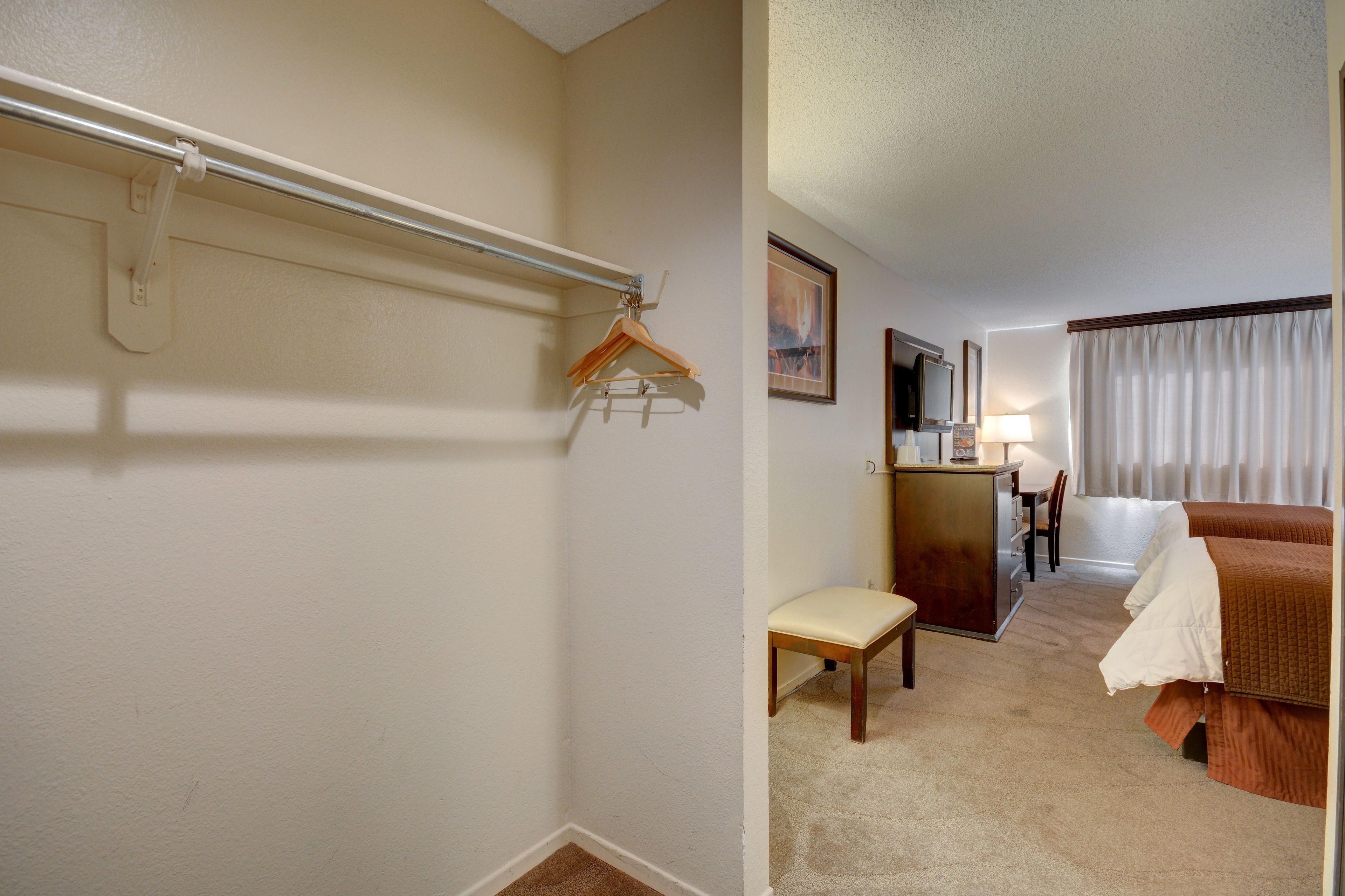 A hotel room with a bed, a desk with a chair, a hanging coat rack, and a small bench.