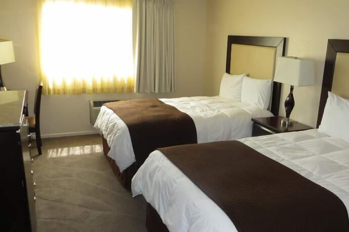 Habitación de hotel con dos camas, un escritorio, una silla y una ventana con cortinas.